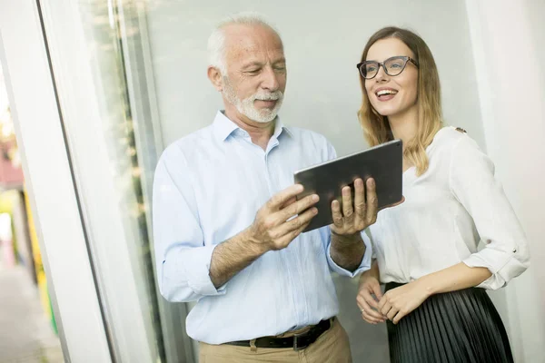 Senior man presenting data to young woman on digital tablet at office