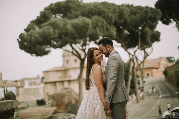 若い魅力的な新婚夫婦ウォーキングや婚礼の日の背景に美しいと古代のアーキテクチャを持つローマでポーズをとって — ストック写真
