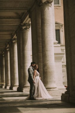 Yeni evli iki genç çekici yürüyor ve düğün günlerinde arka planda güzel ve antik mimari ile Roma'da poz