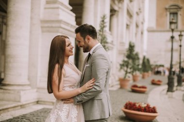 Yeni evli iki genç çekici yürüyor ve düğün günlerinde arka planda güzel ve antik mimari ile Roma'da poz