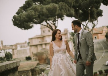 Yeni evli iki genç çekici yürüyor ve düğün günlerinde arka planda güzel ve antik mimari ile Roma'da poz