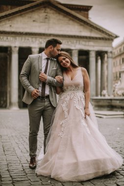 Yeni evli iki genç çekici yürüyor ve düğün günlerinde arka planda güzel ve antik mimari ile Roma'da poz