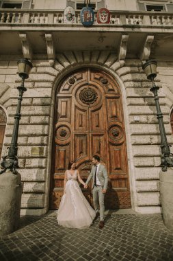 Yeni evli iki genç çekici yürüyor ve düğün günlerinde arka planda güzel ve antik mimari ile Roma'da poz