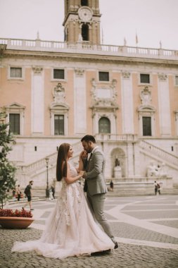 Yeni evli iki genç çekici yürüyor ve düğün günlerinde arka planda güzel ve antik mimari ile Roma'da poz