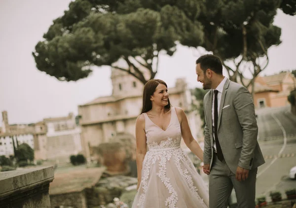 Yeni evli iki genç çekici yürüyor ve düğün günlerinde arka planda güzel ve antik mimari ile Roma'da poz