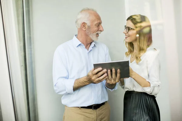 Senior man presenting data to young woman on digital tablet at office