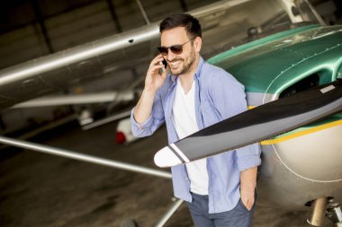 Hangarda uçak kontrol ve cep telefonuyla genç yakışıklı genç pilot