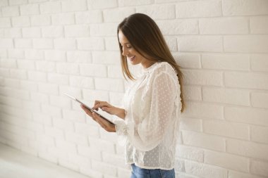 Genç ve güzel kadın tarafından beyaz duvar dijital tablet kullanma