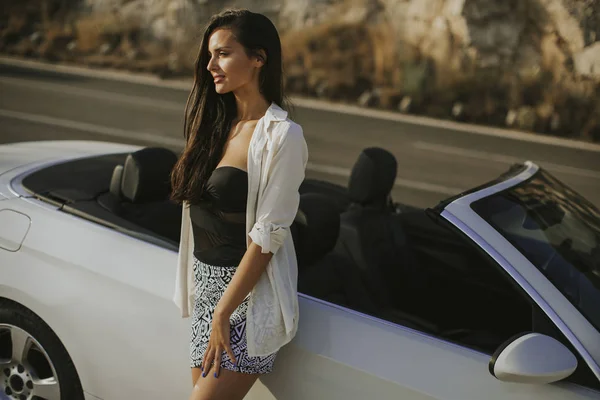 海で晴れた日に白のカブリオレの車で立っているかなり若い女性 — ストック写真