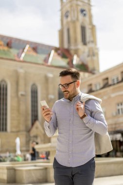 Neşeli genç adam cep telefonu kentsel çevre güneşli gün kullanır