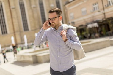 Neşeli genç adam cep telefonu kentsel çevre güneşli gün kullanır