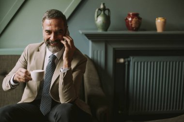 Kahve içme ve cep telefonuyla lobisinde yakışıklı üst düzey işadamı portresi