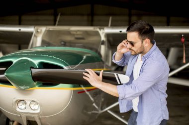 Hangarda uçak kontrol ve cep telefonuyla genç yakışıklı genç pilot