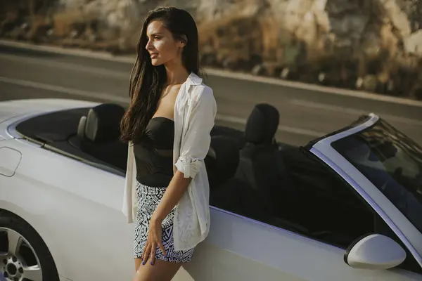 美丽的年轻女子站在白色敞篷车在阳光明媚的一天在海边 — 图库照片