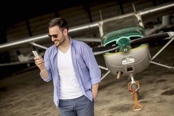 Young Handsome Young Pilot Checking Airplane Hangar Using Mobile Phone — Stock Photo, Image