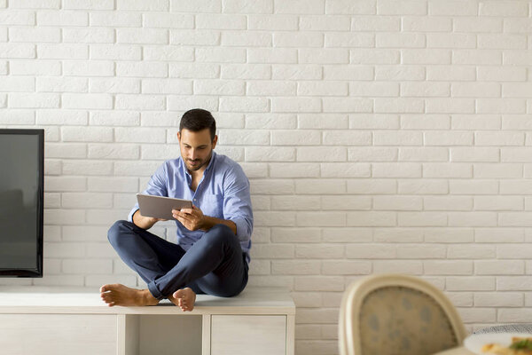 Young man using digital tablet in the room by white wall