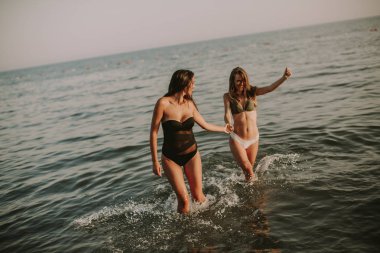 Gün batımında sahilde denizin kenarında eğleniyor iki genç ve güzel kadın