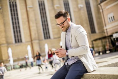 Açık güneşli gün oturup cep telefonunuzla neşeli genç adam portresi