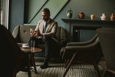 Kahve içme ve cep telefonuyla lobisinde yakışıklı üst düzey işadamı portresi