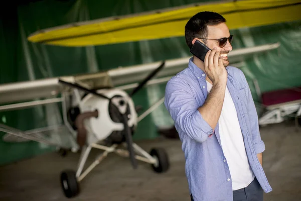 Молодой Красивый Молодой Пилот Проверяет Самолет Ангаре Пользуется Мобильным Телефоном — стоковое фото