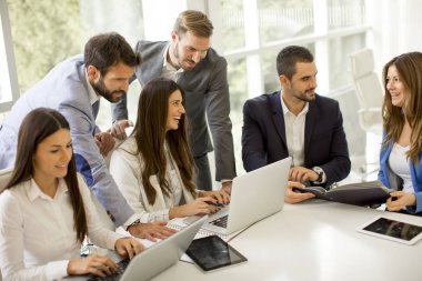 Girişim ekibi, modern parlak ofis içinde toplantı ve dizüstü bilgisayar üzerine çalışıyor