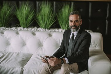 Modern ofisinde oturan dijital tablet ile kendine güvenen üst düzey iş adamı