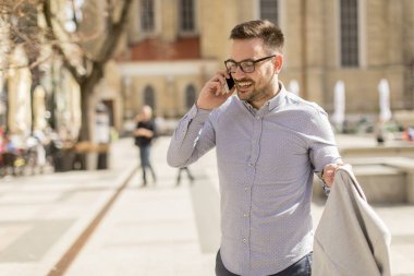 Neşeli genç adam cep telefonu kentsel çevre güneşli gün kullanır