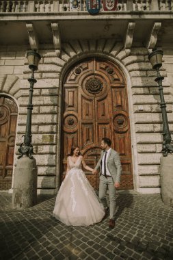 Yeni evli iki genç çekici yürüyor ve düğün günlerinde arka planda güzel ve antik mimari ile Roma'da poz