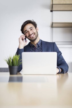 Dizüstü bilgisayarda çalışan ve modern ofis cep telefonu konuşurken genç işadamı