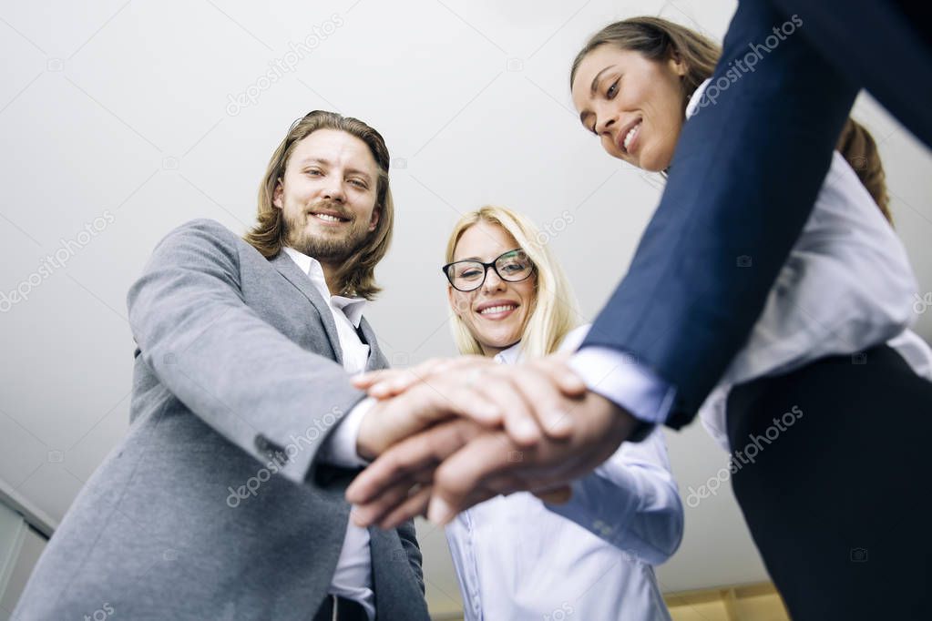 Closeup of young coworkers putting hands together as symbol of unity in the office