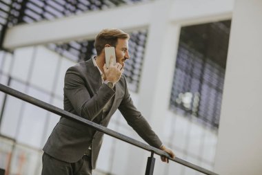 Gri takım elbise giyiyor ve onun smartphone modern ofis veya gökdelenler yanında dururken tutan genç başarılı iş adamı