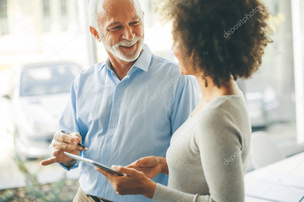 Senior man presenting data to young woman on digital tablet at office