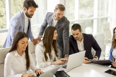 Girişim ekibi, modern parlak ofis içinde toplantı ve dizüstü bilgisayar üzerine çalışıyor