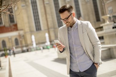 Neşeli genç adam cep telefonu kentsel çevre güneşli gün kullanır