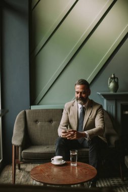 Kahve içme ve cep telefonuyla lobisinde yakışıklı üst düzey işadamı portresi