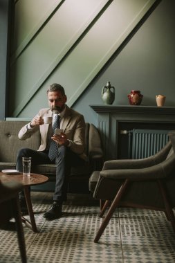 Kahve içme ve cep telefonuyla lobisinde yakışıklı üst düzey işadamı portresi