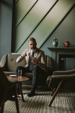 Kahve içme ve cep telefonuyla lobisinde yakışıklı üst düzey işadamı portresi