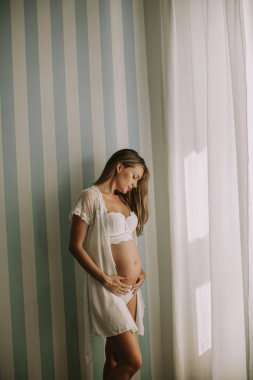 Pencerenin kenarında duran genç ve güzel hamile kadın