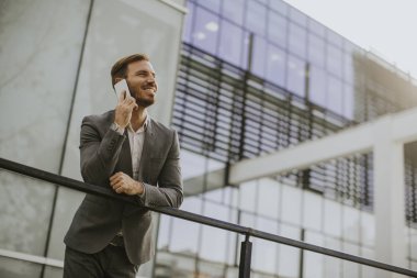 Gri takım elbise giyiyor ve onun smartphone modern ofis veya gökdelenler yanında dururken tutan genç başarılı iş adamı