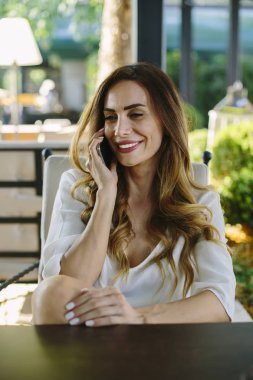 Kafede oturan ve cep telefonunuzun yaz gününde genç kadın