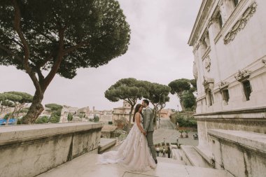 Yeni evli iki genç çekici yürüyor ve düğün günlerinde arka planda güzel ve antik mimari ile Roma'da poz