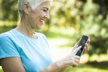 Cep telefonuyla parkta sportif kadın kıdemli portresi