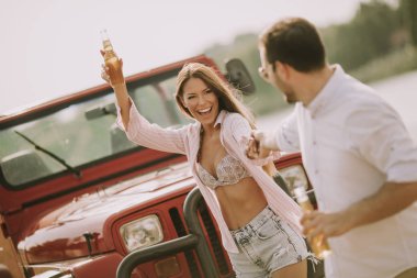 Genç kadın ve adam arabanın yakınında açık yaz gününde eğleniyor