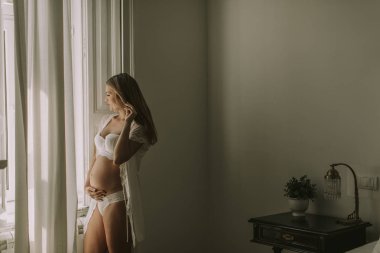 Pencerenin kenarında duran genç ve güzel hamile kadın