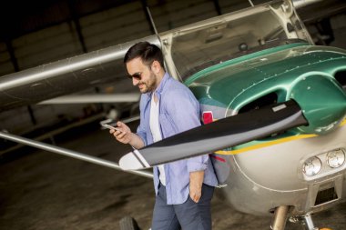 Hangarda uçak kontrol ve cep telefonuyla genç yakışıklı genç pilot