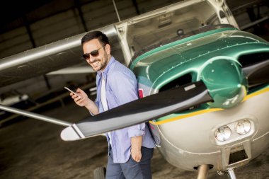 Hangarda uçak kontrol ve cep telefonuyla genç yakışıklı genç pilot