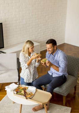 Sevgi dolu bir çift evde dinleniyor ve lezzetli pizzalar yiyor.