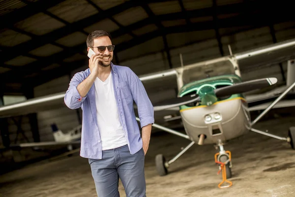 Jovem Bonito Jovem Piloto Verificando Avião Hangar Usando Telefone Celular — Fotografia de Stock