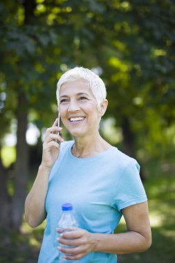 Cep telefonuyla parkta sportif kadın kıdemli portresi