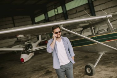 Hangarda uçak kontrol ve cep telefonuyla genç yakışıklı genç pilot